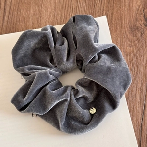 Dettaglio dell'elastico scrunchie in velluto grigio scuro con ciondolo in metallo dorato