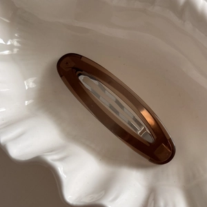 Macro shot of a vintage amber brown oval hair clip on a white decorative shell tray