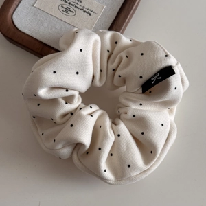 Détail d'un chouchou en tissu crème à pois noirs avec étiquette de logo brodée