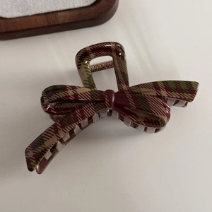 Detail of red and green plaid bow hair claw clip showing acetate texture and metal spring