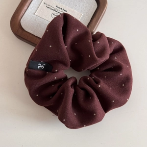 Gros plan sur un chouchou bordeaux à pois avec une étiquette tissée logo nœud noir