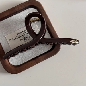 Detail of a dark brown glossy hair claw clip with golden French lettering on wood tray