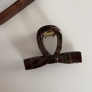 Detailed close-up of dark red and green plaid hair claw clip with gold metal spring