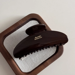 Detail view of large dark brown resin hair claw clip with golden logo on wooden display