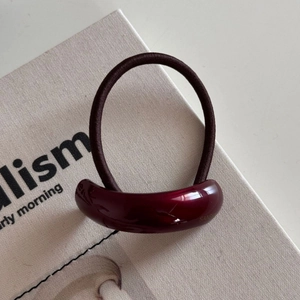 Close-up of a burgundy resin curved charm on a thick brown elastic hair scrunchie