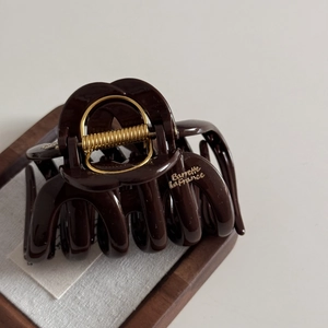 Close-up of a large chocolate brown hair claw clip with golden lettering on a wooden tray