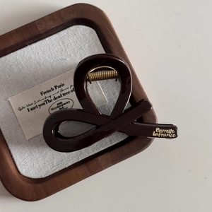 Detail of a chocolate brown shark hair claw with a gold-tone French inscription label