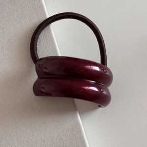 Detail of high-elasticity hair tie with dark red curved ornament and golden logo accent