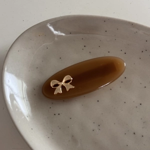 Close-up of brown acetate oval hair clip with elegant golden metal bow detail