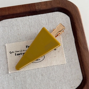 Close-up of mustard yellow triangular acrylic hair clip with gold metal base on wood