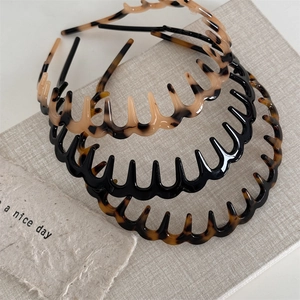Three-piece set of wavy acetate headbands in tortoiseshell and black on a textured book