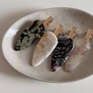 Detail of four acetate hair clips with ink patterns on a ceramic display tray