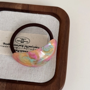 Close-up of crescent-shaped aurora resin pendant on a brown elastic hair tie