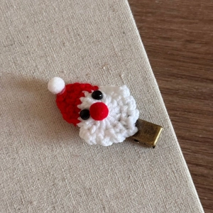 Detailed close-up of a handmade knitted Santa Claus hair clip with soft yarn texture