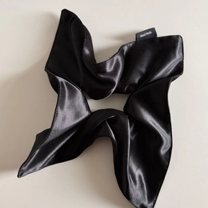 Detail of a handmade black satin silk scrunchie with a visible hand made textile label