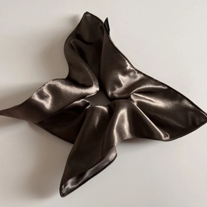 Close-up of a large dark brown satin scrunchie with silk gloss and a small woven label