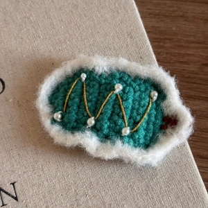Detail of green handmade knit Christmas hair clip with white plush trim and faux pearls