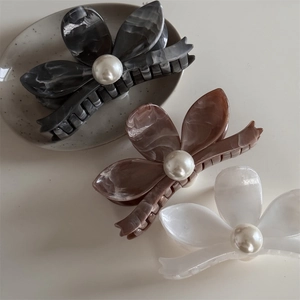 Three acetate flower hair claws with marble texture and pearls on a ceramic plate