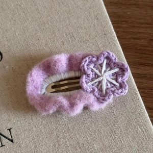 Close-up of a handmade purple knitted hair clip with a delicate white floral accent