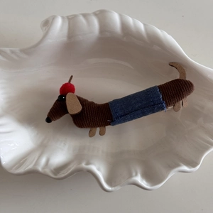 Detailed view of cartoon dachshund hair clip with fabric texture in a white shell dish