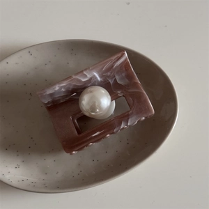 Detail of marble pattern hair claw clip with large pearl on minimalist ceramic tray
