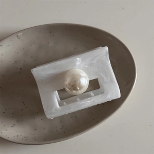 Detail of white marble textured hair claw clip with a glossy pearl on a ceramic plate