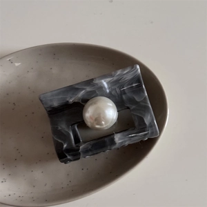 Detail of marble pattern hair claw clip with a large pearl on a ceramic tray