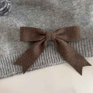 Close-up of deep brown knitted bow hair clip with ribbed texture on gray sweater
