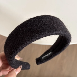 Close-up of a wide black wool fabric headband featuring a stitched handmade label