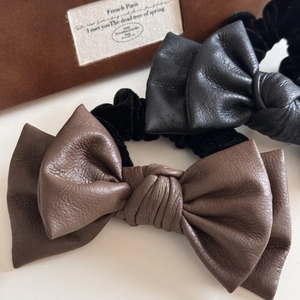 Close-up of black and brown leather bow scrunchies with fine texture and elastic velvet band