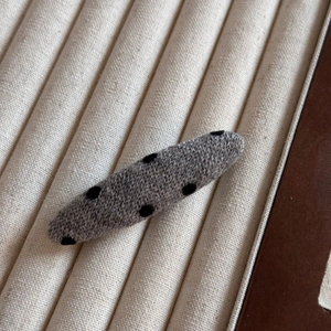Vue détaillée de la pince à cheveux en tricot gris à pois noirs et texture douce