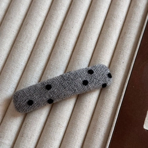 Gros plan d'une pince à cheveux rectangulaire grise à pois noirs sur un plateau beige