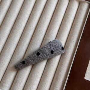 Détail d'une pince à cheveux grise tricotée à pois noirs sur un présentoir à bijoux