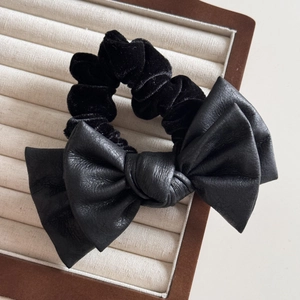 Close-up of a premium black velvet scrunchie featuring a large leather bow detail