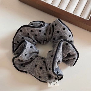 Détail d'un chouchou en tricot gris à pois noirs avec une étiquette de visage souriant