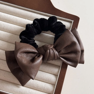Detail of premium brown leather bow and black velvet scrunchie on a beige tray