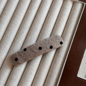 Gros plan d'une pince à cheveux tricotée beige à pois noirs sur un support en velours