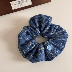Detail of blue tweed scrunchie featuring a classic button accent and rich woven texture