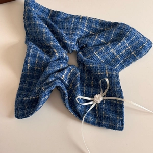Detail of tweed scrunchie in denim blue with a white ribbon bow and resin flower