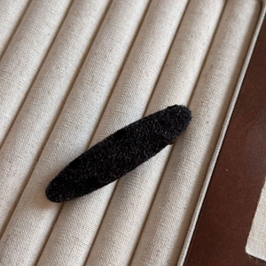 Détail d'une pince à cheveux ovale en tissu noir avec texture douce sur plateau velours