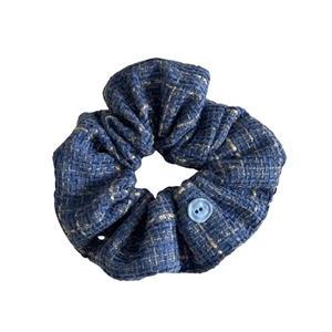Denim blue tweed scrunchie with gold threads and a round button on a white background
