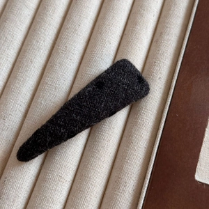 Détail d'une pince à cheveux triangulaire en tissu noir avec une texture tricotée douce