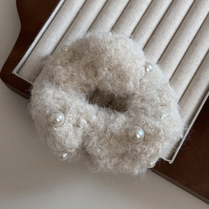 Détail d'un chouchou en peluche blanche avec perles sur un plateau de présentation