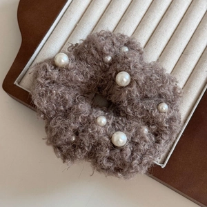 Détail d'un chouchou en peluche marron avec perles blanches et texture laine d'agneau