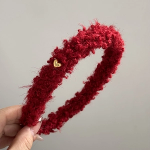 Gros plan d'un serre-tête en peluche rouge bouclée avec détail de cœur en métal doré