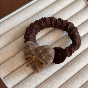 Close-up of brown plaid felt heart hair tie with bow on beige striped jewelry tray