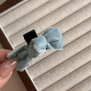 Macro detail of soft light blue velvet bow hair clip with black plastic duckbill clip
