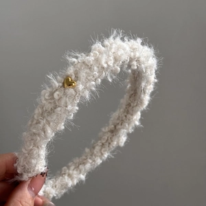 Gros plan sur un serre-tête en peluche crème avec un détail de breloque cœur doré