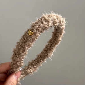 Détail d'un serre-tête en peluche kaki orné d'un pendentif en métal doré en forme de cœur