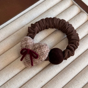 Detail of a brown plaid heart and velvet ball on a ruffled scrunchie in a jewelry tray